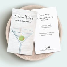 two business cards sitting on top of a plate next to a glass with an olive in it