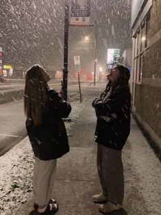 two women standing on the sidewalk in the snow looking at each other with their eyes closed