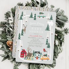 a christmas themed wedding card with trees, houses and cars on the front is surrounded by greenery