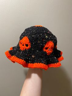 a hand is holding up a crocheted hat with orange and black decorations on it