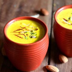 two red bowls filled with soup on top of a wooden table next to almonds