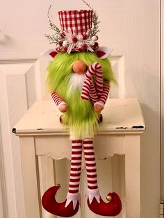 a green elf doll sitting on top of a white table next to a red and white door