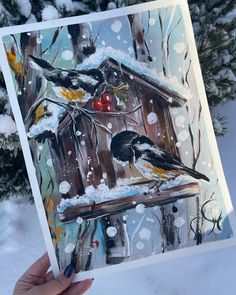 a person holding up a card with birds on it in front of snow covered trees