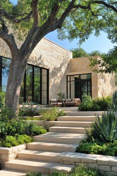 a stone house with steps leading to the front door and patio area, surrounded by greenery