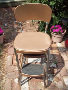 a brown chair sitting on top of a brick floor next to potted plants and flowers