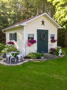 a small white shed sitting in the middle of a lush green yard with flowers and potted plants