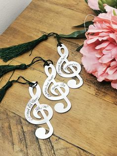 three silver musical notes with tassels on a wooden table next to pink flowers