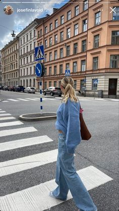 a woman walking across a cross walk in front of tall buildings on a city street