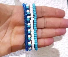 a hand holding three bracelets with white and blue beads on each one strand,