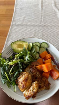 a white plate topped with meat and veggies next to a knife and fork