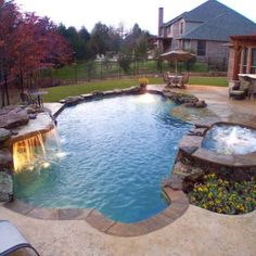 an outdoor swimming pool with waterfall and fire pit in the back yard, surrounded by landscaping