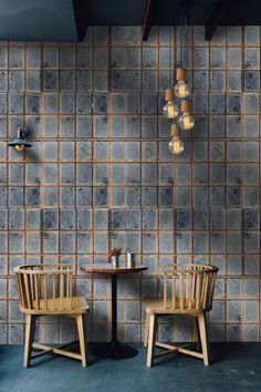 two wooden chairs sitting next to each other in front of a wall with blue tiles