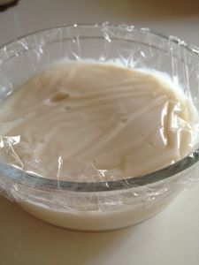 a glass bowl filled with cream sitting on top of a white counter next to a plastic wrapper