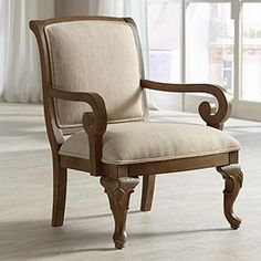 a wooden chair with beige upholstered seat and arm rests in front of a window