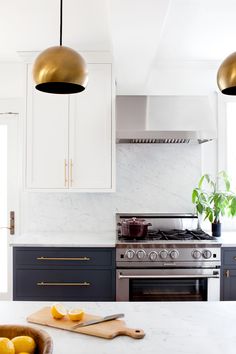 a kitchen with marble counter tops and gold pendant lights hanging over the stove, along with two yellow lemons on a cutting board