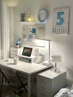 a white desk topped with a laptop computer next to a wall mounted calendar and lamp