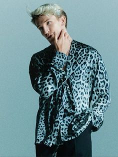 a man with blonde hair wearing a leopard print shirt and black pants, posing for the camera