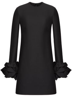 a black dress with ruffles on the sleeves and cuffs, in front of a white background