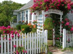 a white picket fence with pink flowers growing on it and a house in the background