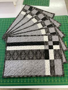 four quilts laid out on top of a green cutting board with ruler and measuring tape