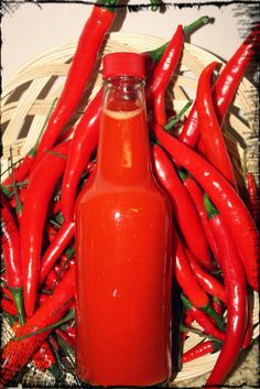 a bottle of hot sauce sitting next to some chili peppers on a wicker basket