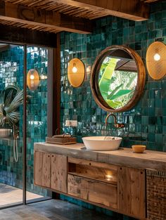 a bathroom with green tiled walls and wooden vanity, round mirror on the wall above it