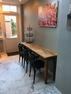 a dining room table and chairs in front of a door with a painting on the wall