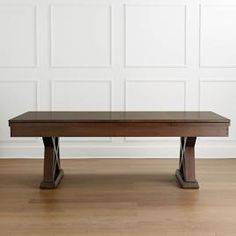 a wooden table sitting on top of a hard wood floor next to a white wall