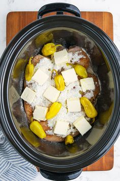 a crock pot filled with food sitting on top of a wooden cutting board