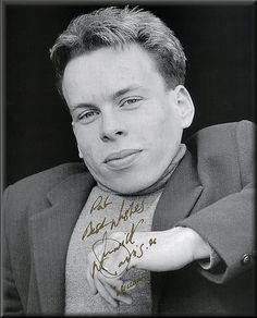 a black and white photo of a man with his hand on his chest, wearing a suit