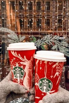 two red starbucks cups sitting next to each other on top of a table covered in snow