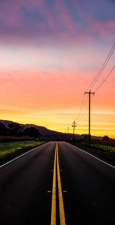 the sun is setting over an empty road with power lines in the distance and telephone poles on either side