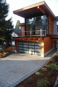 a modern house with wood and glass on the top floor, surrounded by brick pavers