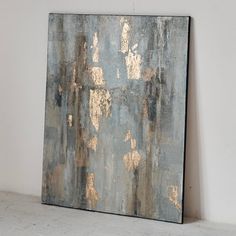 an abstract painting with gold paint on it in a white walled room next to a wall