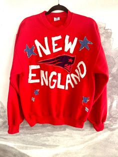 Upcycled Jerzees crew neck with distressed New England Patriots motif. This red white and blue pullover is perfect for any patriotic event outside of football season, or showing off at a game. The star details stand out with distressed upcycled denim patches that will only look cooler with each wear. *GrandmasGarbo is not affiliated, sponsored, endorsed, and/or licensed by the NFL, MLB, NHL, NBA, NCAA, or any college and/or professional sports team/league. 4th Of July Graphic Print Crew Neck Sweatshirt, Patriotic Crew Neck Sweatshirt With Graphic Print, 4th Of July American Flag Print Crew Neck Sweatshirt, Red Patriotic Top For Fall, Winter Sports Fan Crew Neck Sweatshirt, Winter Crew Neck Sweatshirt For Sports Fans, Red Crew Neck Sweatshirt For Sports Events, Diy Sports Shirts, Red Distressed Crew Neck Top