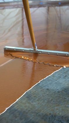 a close up of a person using a broom to clean the floor with brown paint