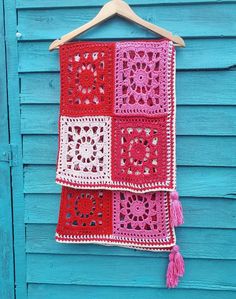 a red and pink crocheted blanket hanging on a blue wall