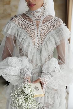 a woman in a white wedding dress holding a book and wearing a bridal veil