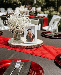 the table is set with red plates, silverware and a photo frame on it