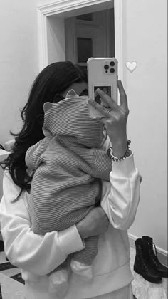 a woman taking a selfie in front of a mirror holding a baby wrapped in a blanket