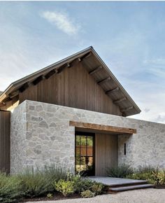 a stone building with a wooden door and window on the front side is surrounded by greenery