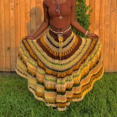 a woman standing in front of a wooden fence wearing a multicolored crocheted skirt