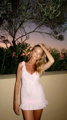 a woman in a white dress posing for the camera at sunset with her hand on her head