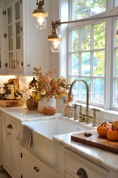 a kitchen with white cabinets and lots of pumpkins on the counter top in front of an open window