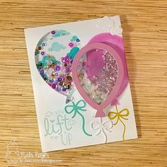 a close up of a card on a wooden surface with balloons and beads in the background