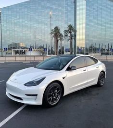 a white car is parked in the parking lot near some tall buildings and palm trees