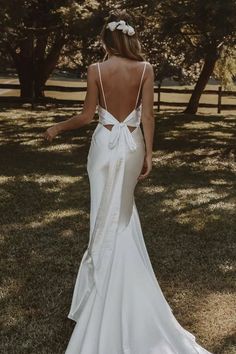 the back of a woman in a white wedding dress standing on grass with trees behind her