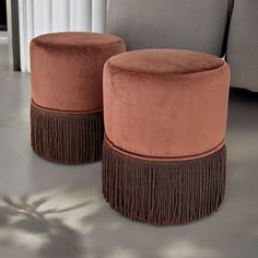 two round stools with fringe trim on them in front of a couch and window