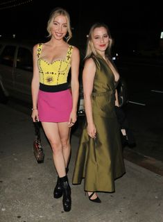 two women in short dresses walking down the street at night, one wearing black and yellow