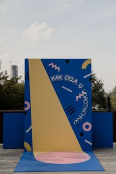 a large blue and yellow sculpture sitting on top of a wooden floor next to trees